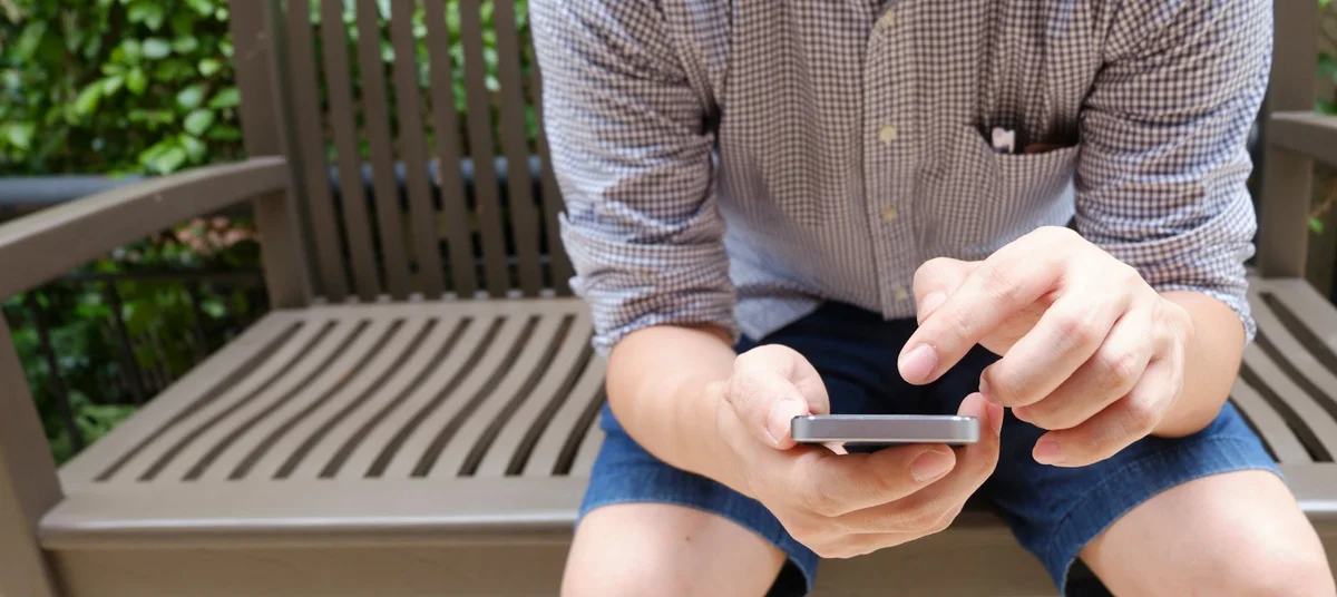 Cómo encontrar tu nicho en TikTok y dejar de publicar al aza... — Man sitting on a bench using a smartphone in a casual outdoor setting.