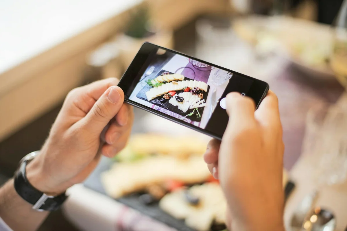 De la visibilidad al ingreso en TikTok — Hands holding a smartphone capturing a photo of a plated dish in a cozy setting.