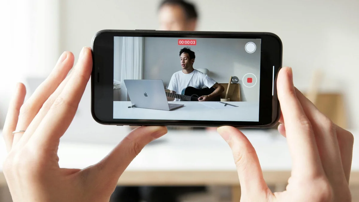 Tu marca personal en TikTok — Man playing guitar while recording a vlog video using a smartphone.