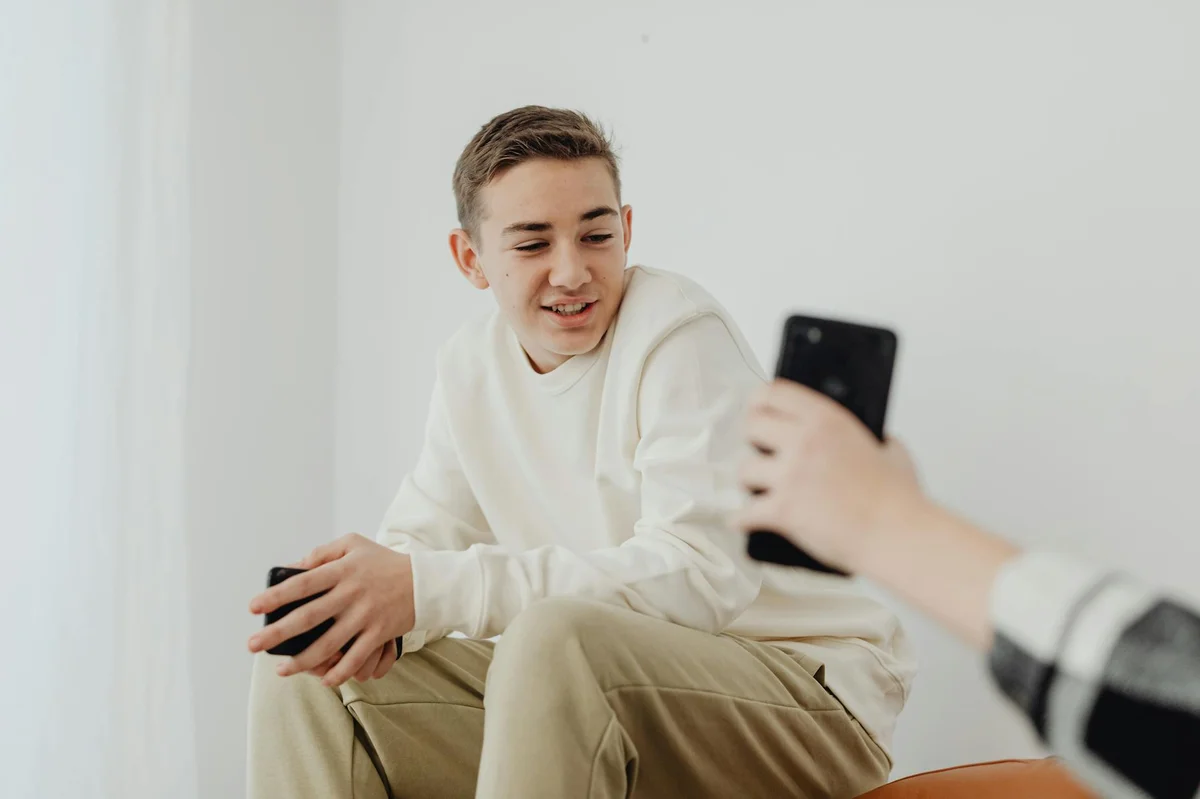 Los formatos de contenido que funcionan en TikTok — A young man dressed casually sits indoors, holding a cellphone, engaging and smi