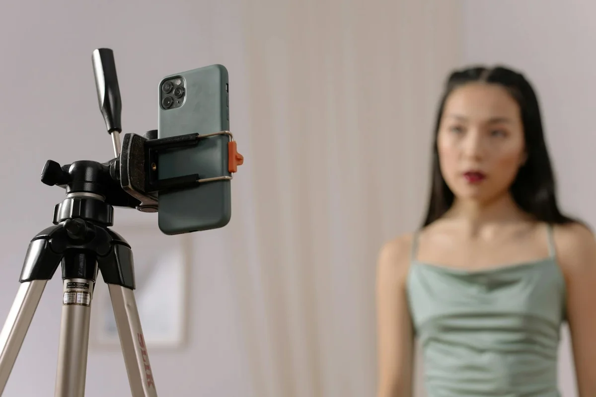 Como funciona el algoritmo de TikTok en 2026 — A woman stands in front of a smartphone set up on a tripod, engaged in vlogging