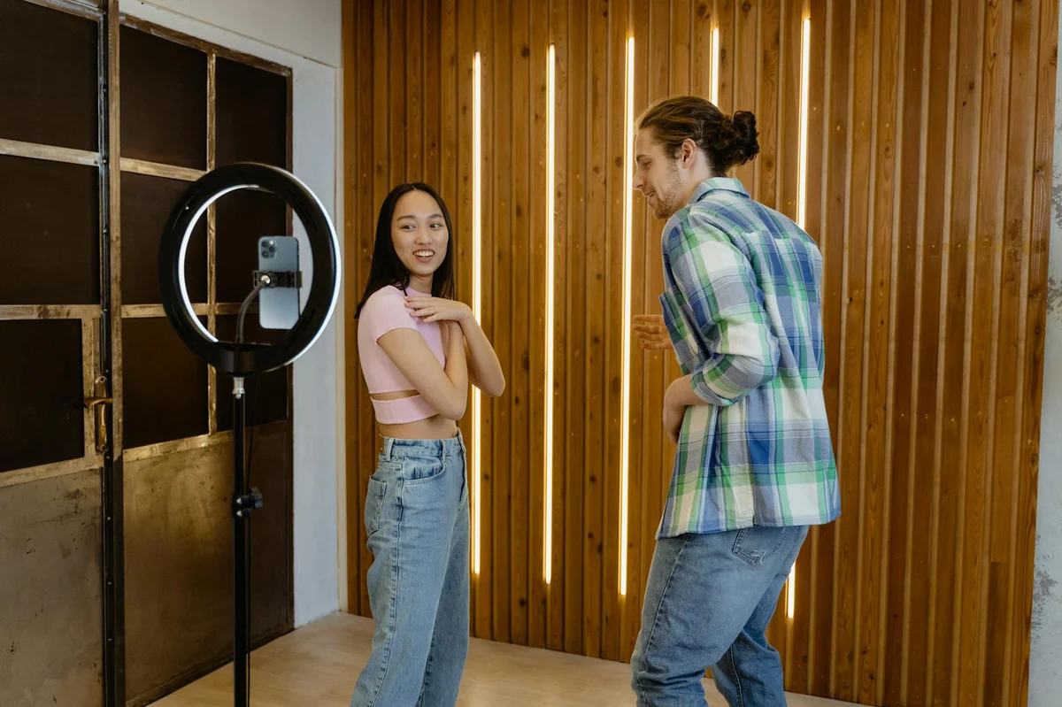 Crear productos y servicios propios desde TikTok — Two young adults having fun dancing in front of a phone camera indoors.