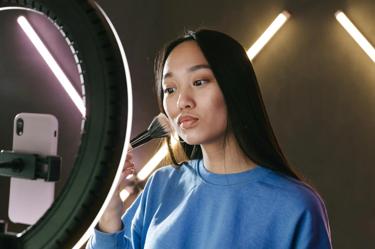 Edicion de video para TikTok: ritmo y cortes — Asian woman filming a makeup tutorial for her vlog using a ring light, emphasizi