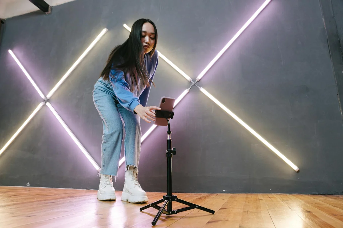 Construir comunidad en TikTok — Young Asian woman setting up smartphone for streaming indoors with neon lights.