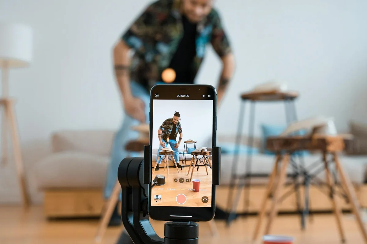 Como crear contenido viral en TikTok — Man recording video content with smartphone on a tripod in a cozy living room.