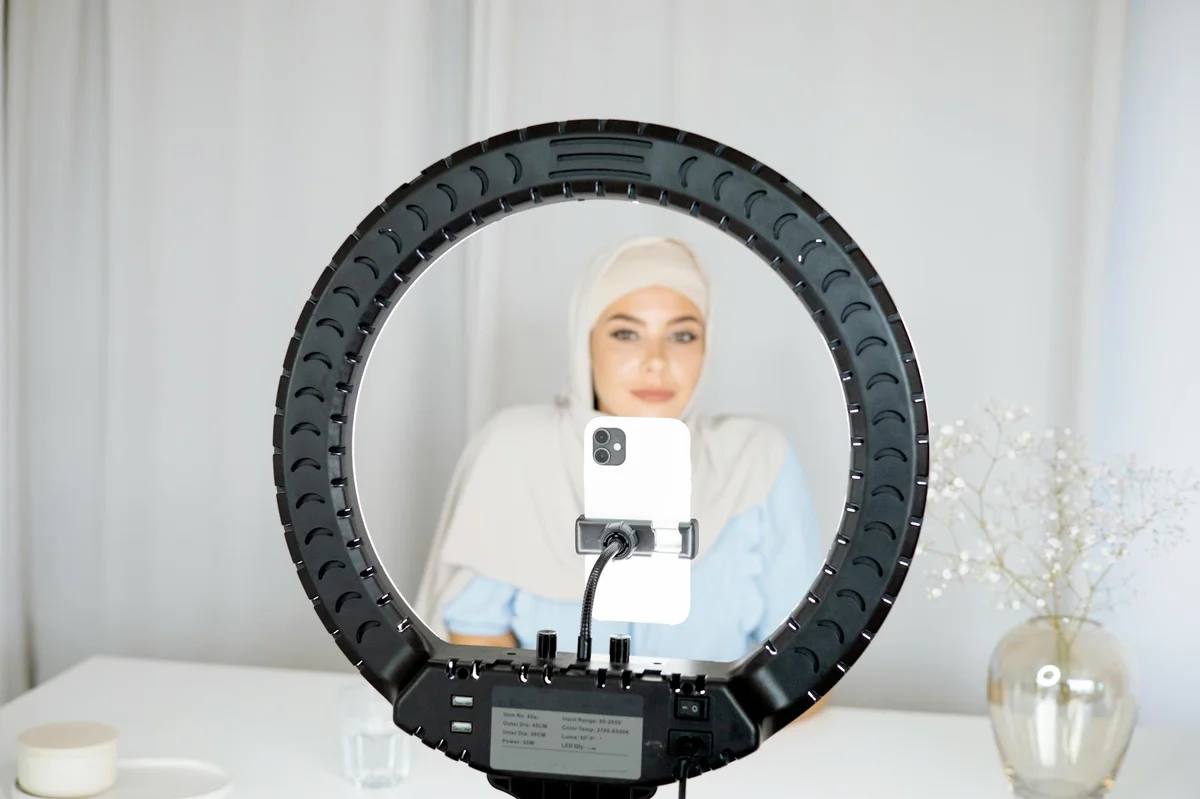 Como optimizar tu perfil de TikTok — A woman in hijab using a ring light to create content indoors with a smartphone.