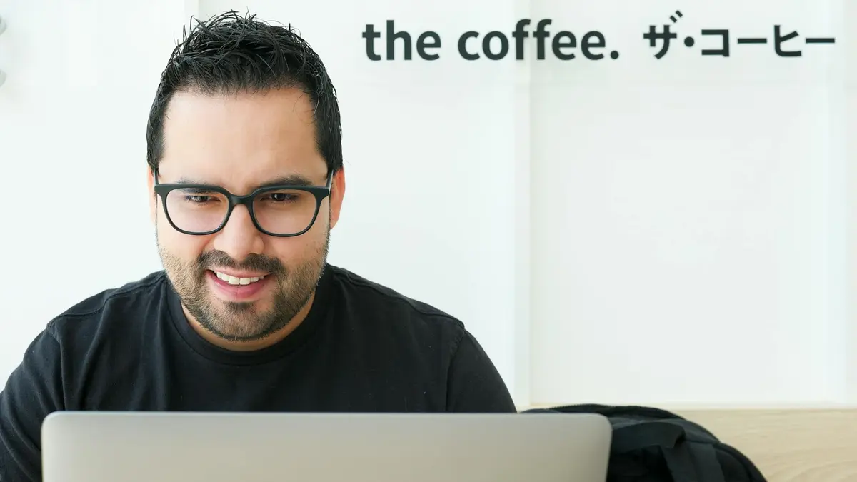 A smiling man using a laptop in a modern coffee shop setting indoors.
