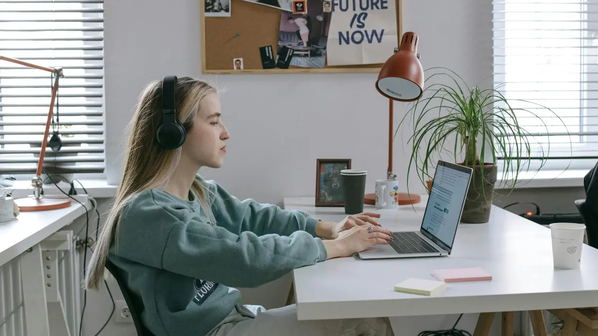 Focused young woman with headphones working on a laptop in a modern office setup.