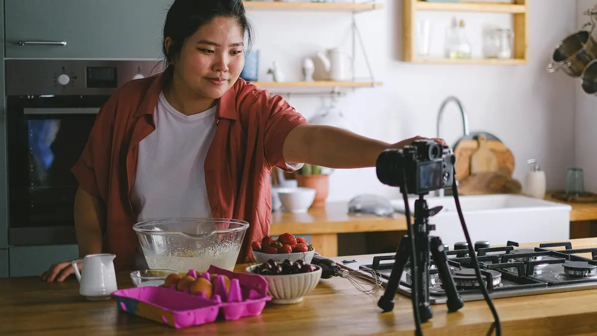 A woman films a cooking vlog in a cozy and modern kitchen with fresh ingredients.