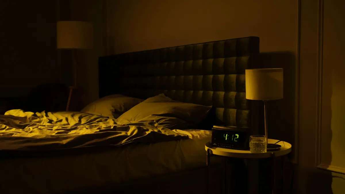 Relaxing dimly lit bedroom with an unmade bed, digital clock displaying 4:12, and warm ambient light