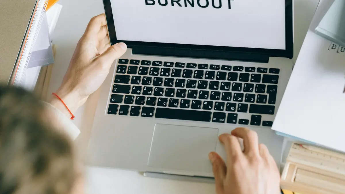 Overhead view of a person typing 'BURNOUT' on a laptop, surrounded by office materials.