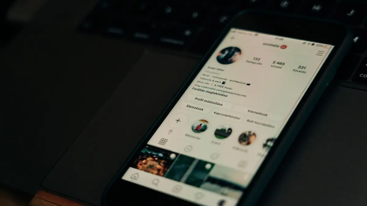 Close-up of smartphone showing a social media profile screen next to a laptop.